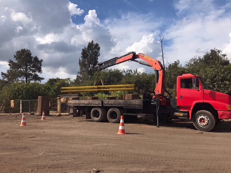 Caminhão munck içando feixe de perfis metálicos em canteiro de obra